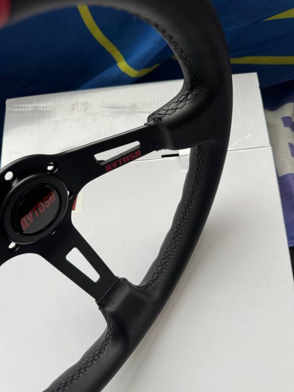 Close-up of the black leather rim, stitching, spoke opening and Avtosh branding.
